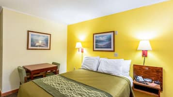 A hotel room with a bed, bedside table with a lamp, a chair, and two framed pictures on the wall.
