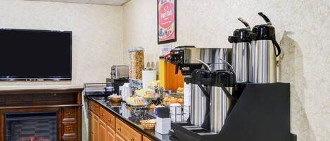 Een keuken met een zwart aanrecht, houten kastjes, een koffieapparaat en een flatscreen televisie.