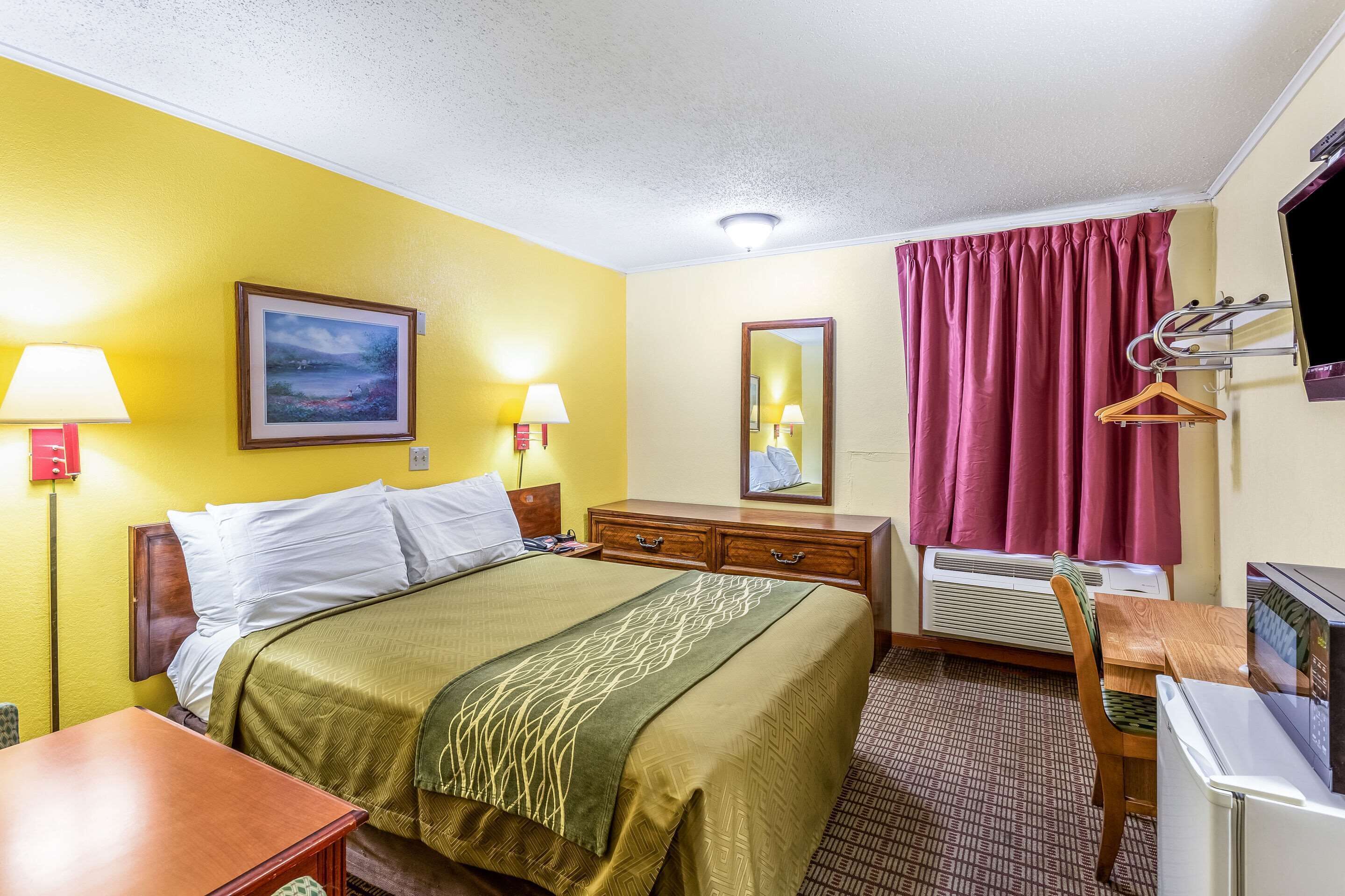 Habitación de hotel con cama, lámparas de noche, cómoda, escritorio, silla, televisor y ventana con cortinas.
