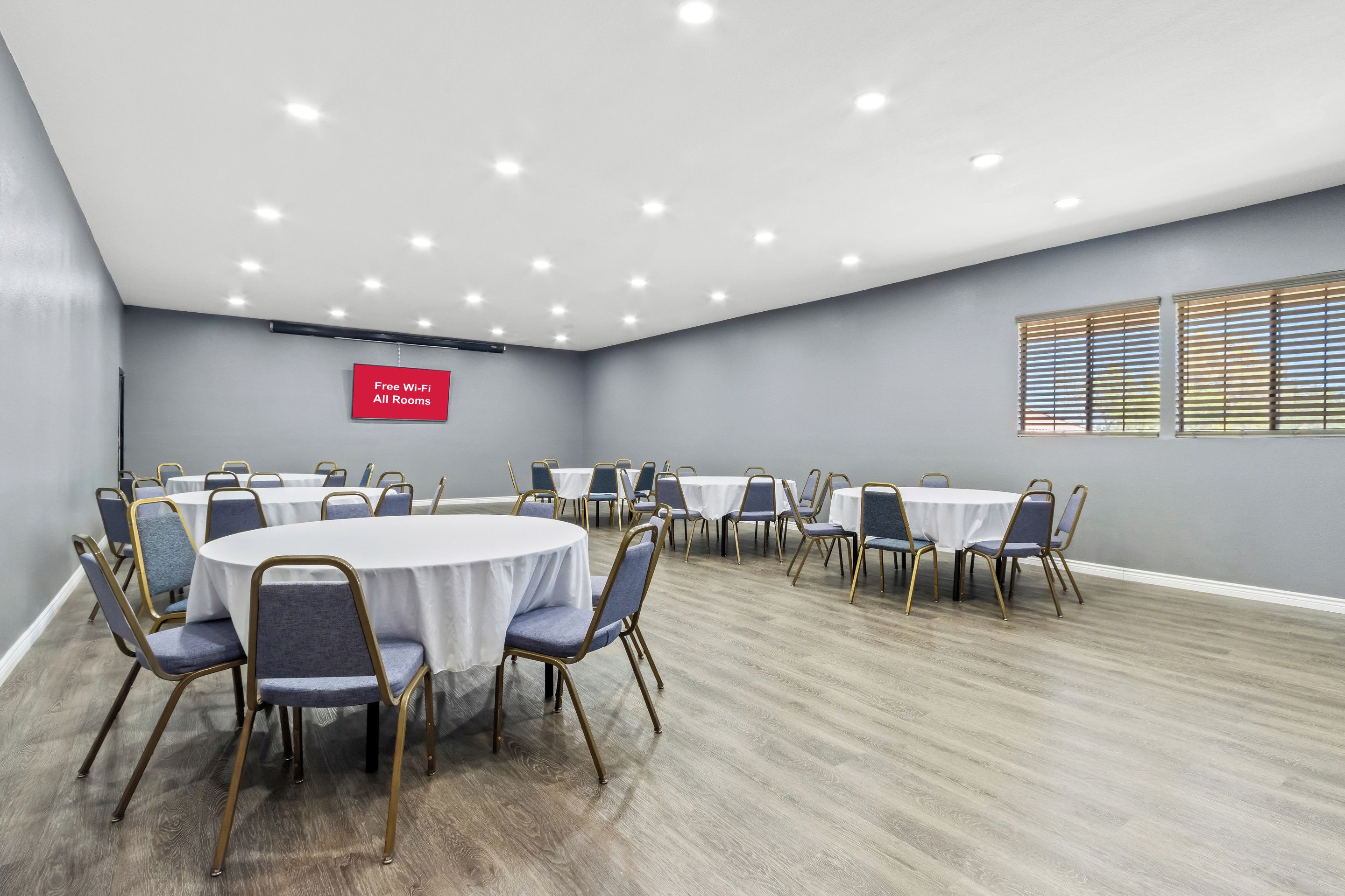 A conference room with round tables and chairs, a sign indicating free Wi-Fi, and a window with blinds.