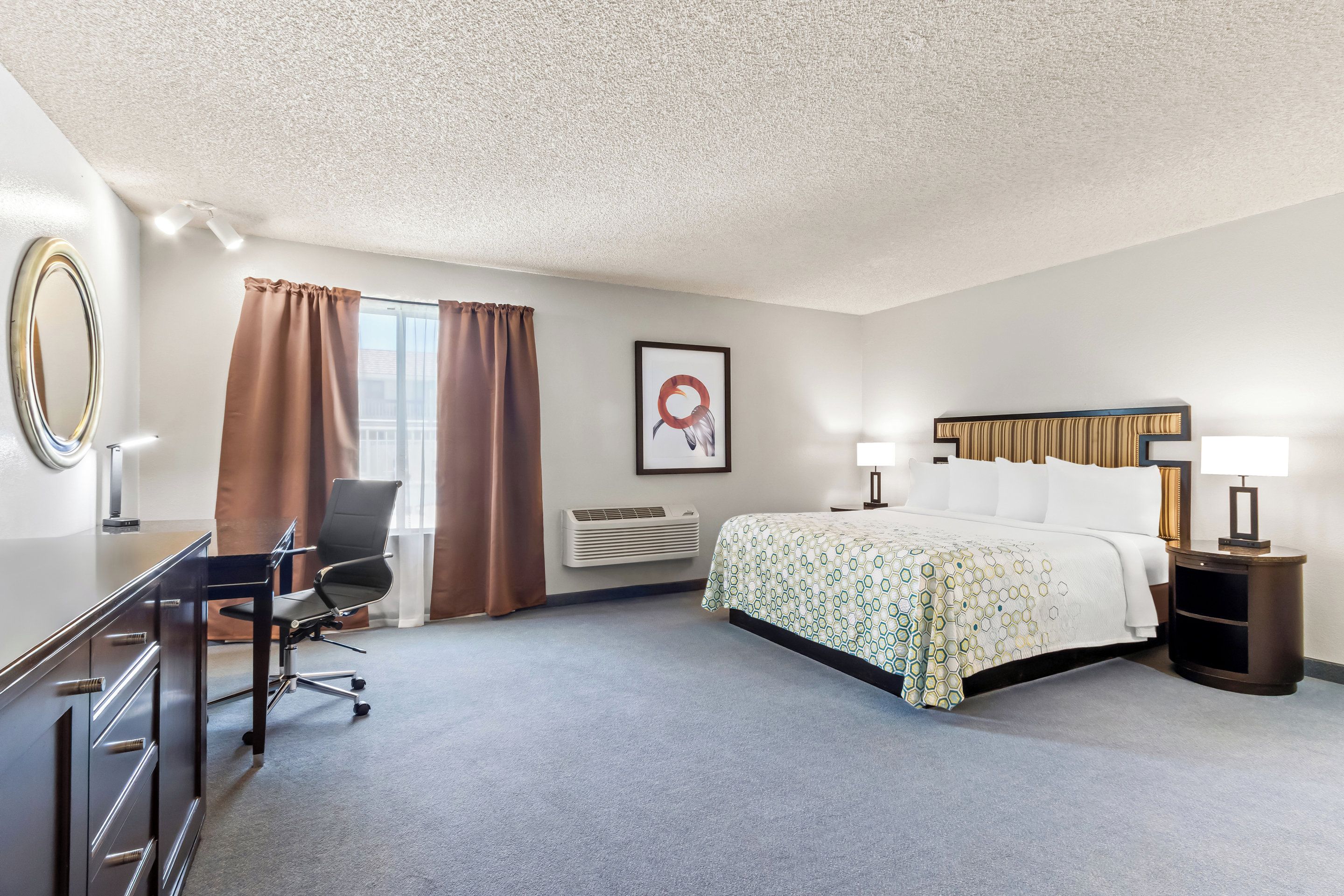 A hotel room with a bed, desk, chair, and a large mirror.