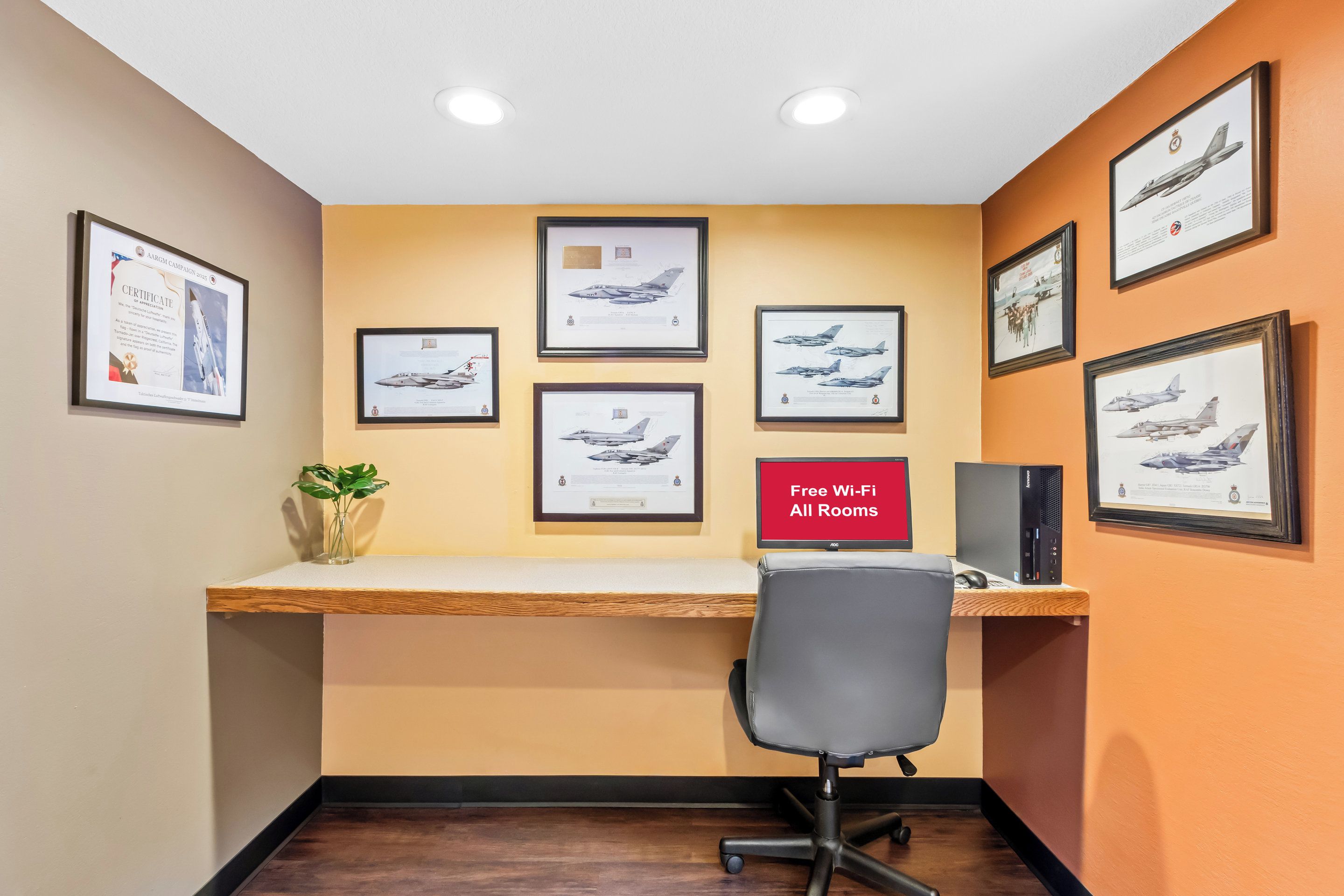 A room with a desk, framed aircraft pictures, a plant, and a sign indicating free Wi-Fi.