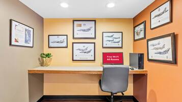 A room with a desk, framed aircraft pictures, a plant, and a sign indicating free Wi-Fi.