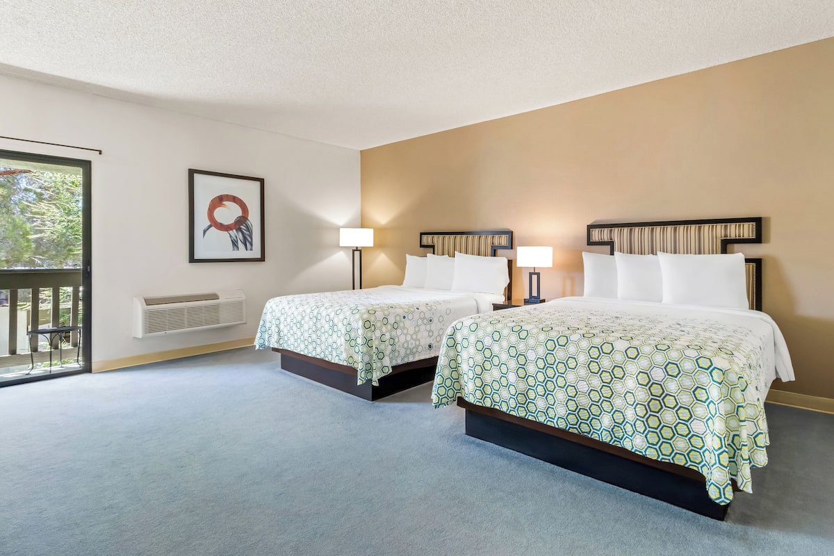A hotel room with two beds, a large window, and a wall-mounted air conditioner.