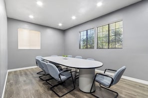 A conference room with a round table, six chairs, and two windows with blinds.