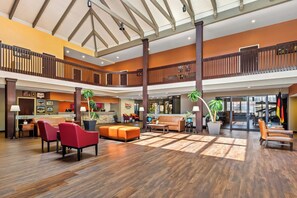 A spacious lobby with a high ceiling, wooden flooring, and a central seating area with red and orange sofas. - HomeTowne Studios by Red Roof Ridgecrest (Ridgecrest)