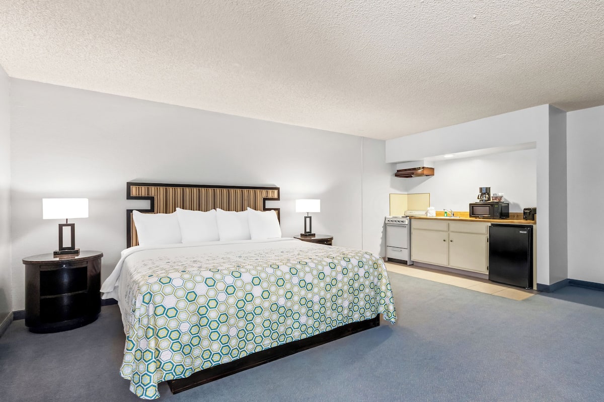 A hotel room with a bed, bedside tables, a small kitchenette, and a bathroom.