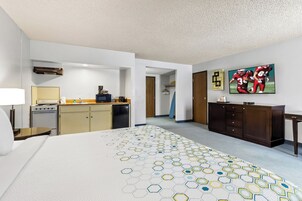 Habitación de hotel con cama, kitchenette, televisor y pasillo que conduce a otra habitación.