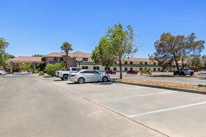 A parking lot with a white car and a truck, a building with a stone facade and a red roof, and trees in the foreground. - HomeTowne Studios by Red Roof Ridgecrest (Ridgecrest)