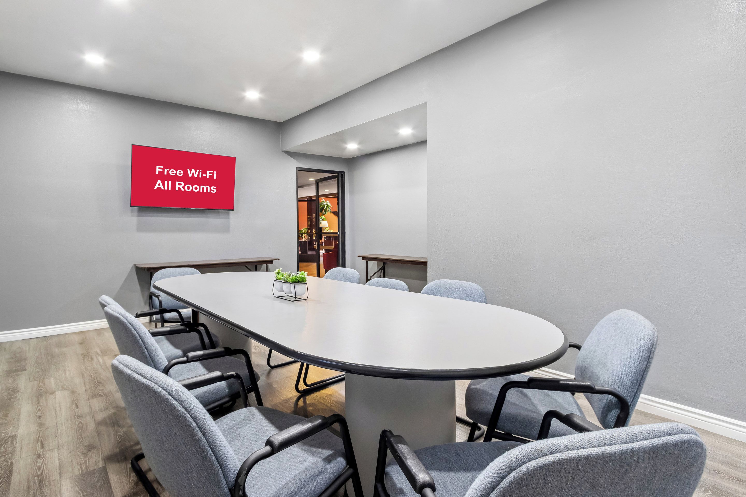 Un salón de conferencias con una larga mesa y seis sillas, un letrero rojo que indica Wi-Fi gratuito, y vistas a otra sala.