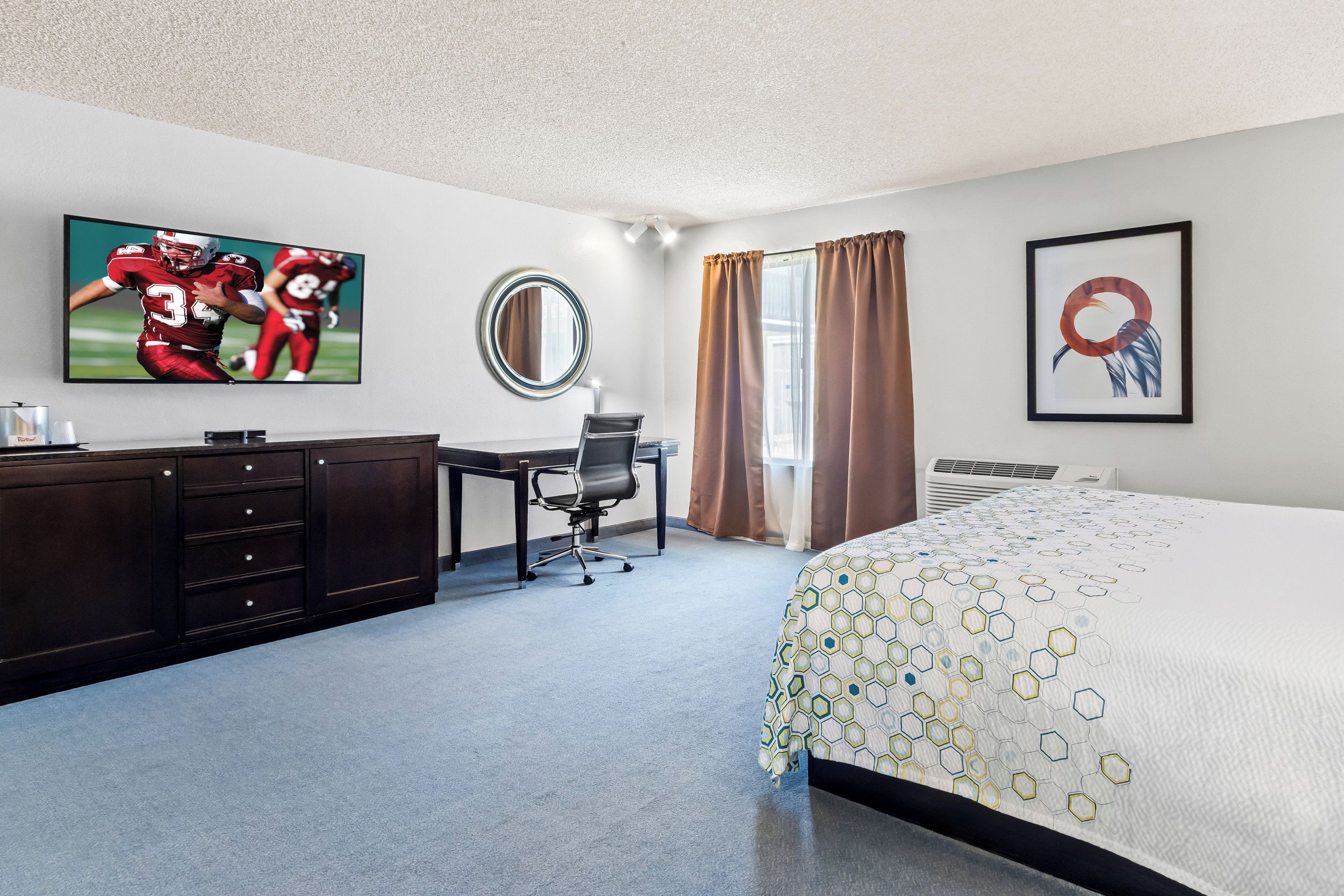 A hotel room with a bed, a desk, a chair, a television, a mirror, and a window with curtains.