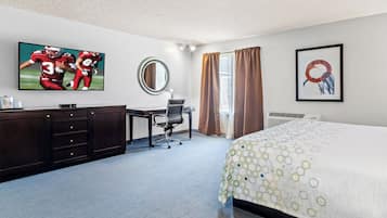 A hotel room with a bed, a desk, a chair, a television, a mirror, and a window with curtains.