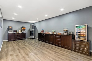 A spacious room with a wooden floor, a dark wooden cabinet with drawers, a refrigerator with a glass door, and a microwave on the counter.