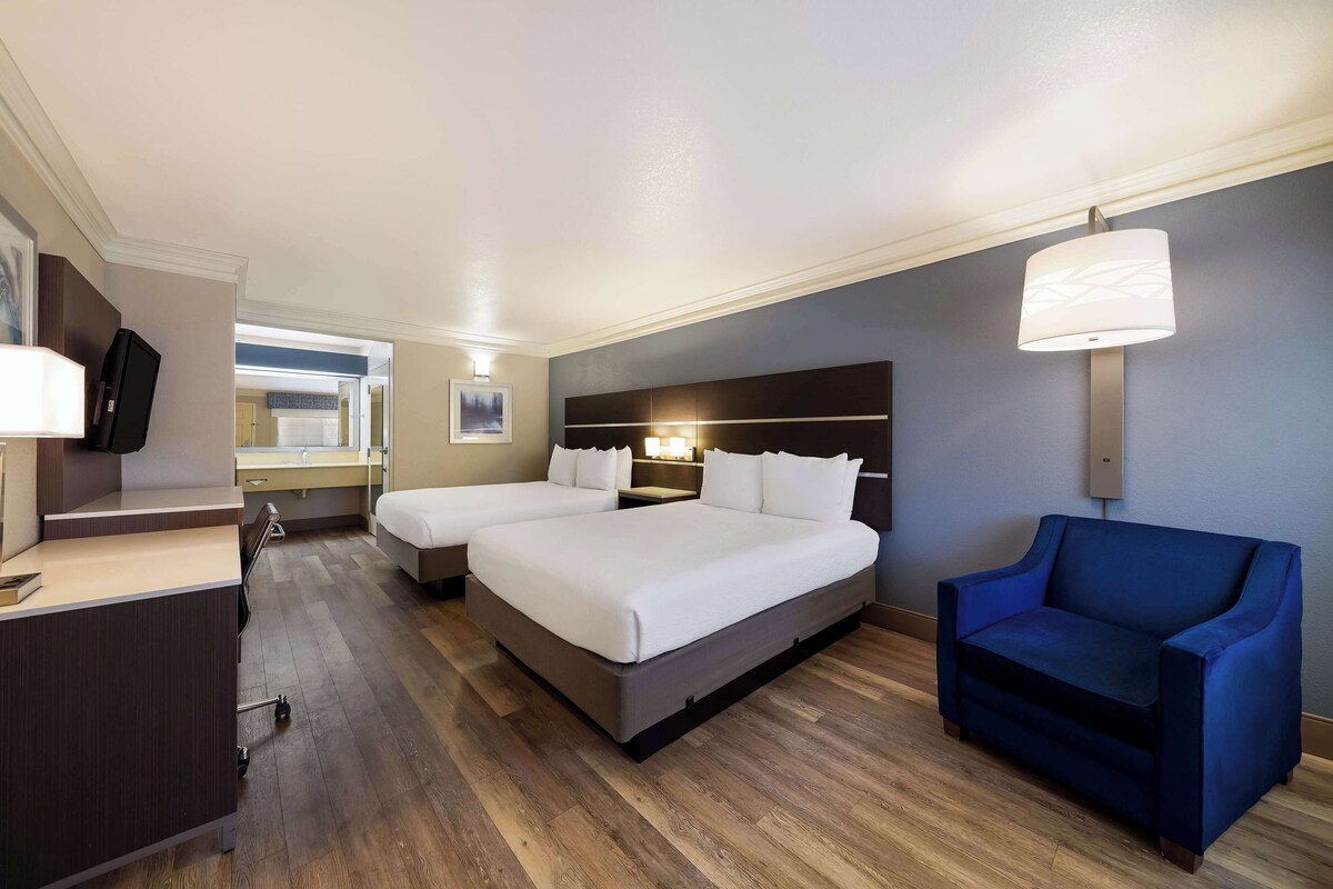 A hotel room with two beds, a desk, a chair, and a large window.