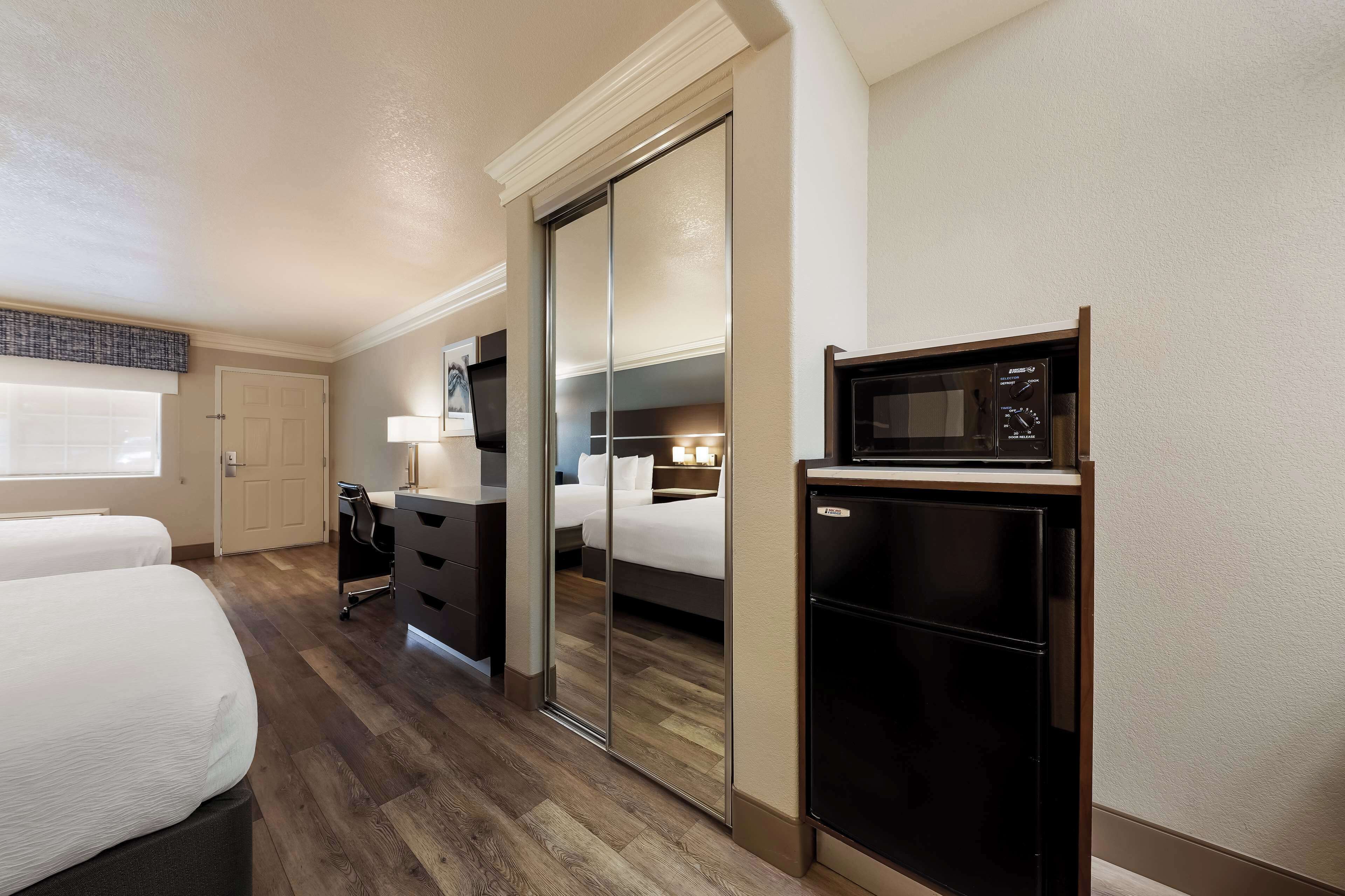 A hotel room with a bed, a desk, a mirror, a microwave, and a refrigerator.