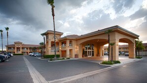 Un hotel con ingresso centrale, diversi balconi e un parcheggio.