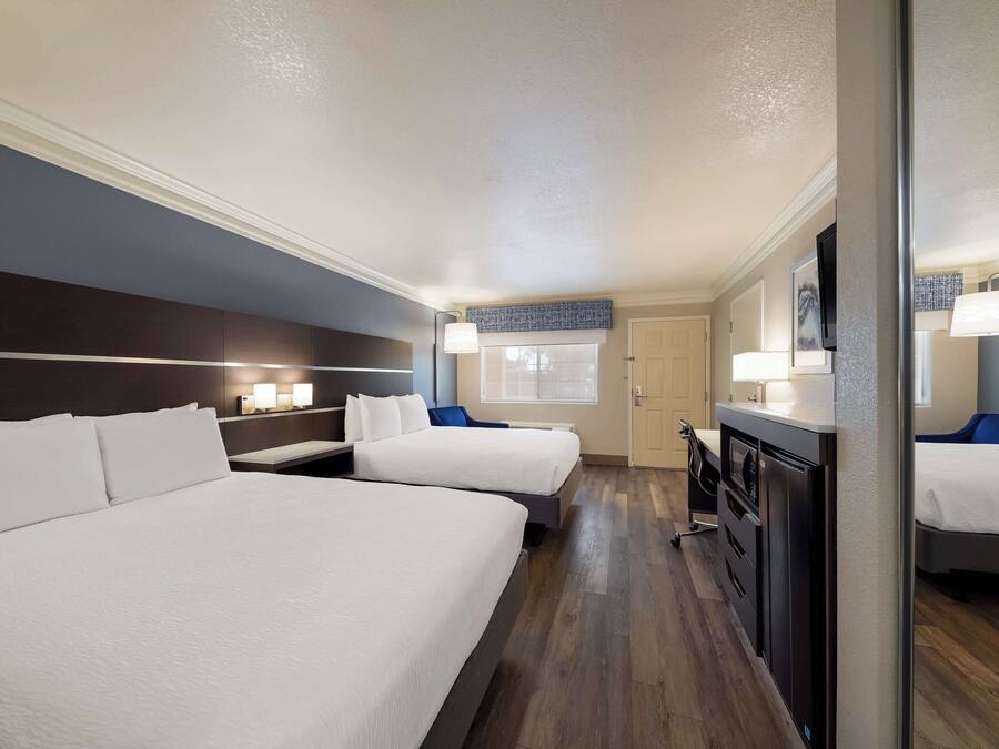 A hotel room with two beds, a desk, a dresser, and a window with a view.