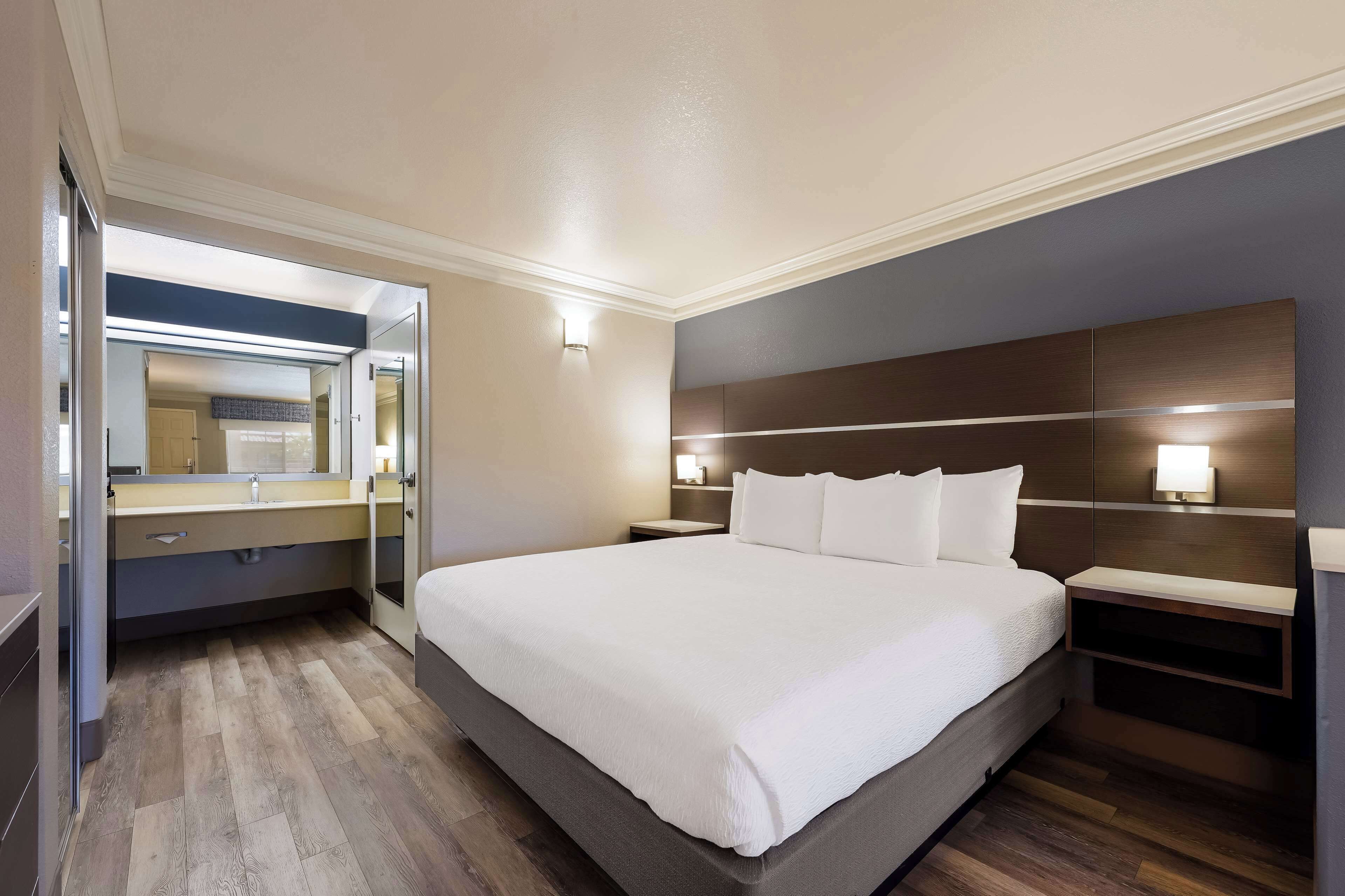 Una habitación de hotel moderna con una cama grande, una mesita de noche, un espejo y una lámpara fijada a la pared.