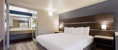 Una habitación de hotel moderna con una cama grande, una mesita de noche, un espejo y una lámpara fijada a la pared.