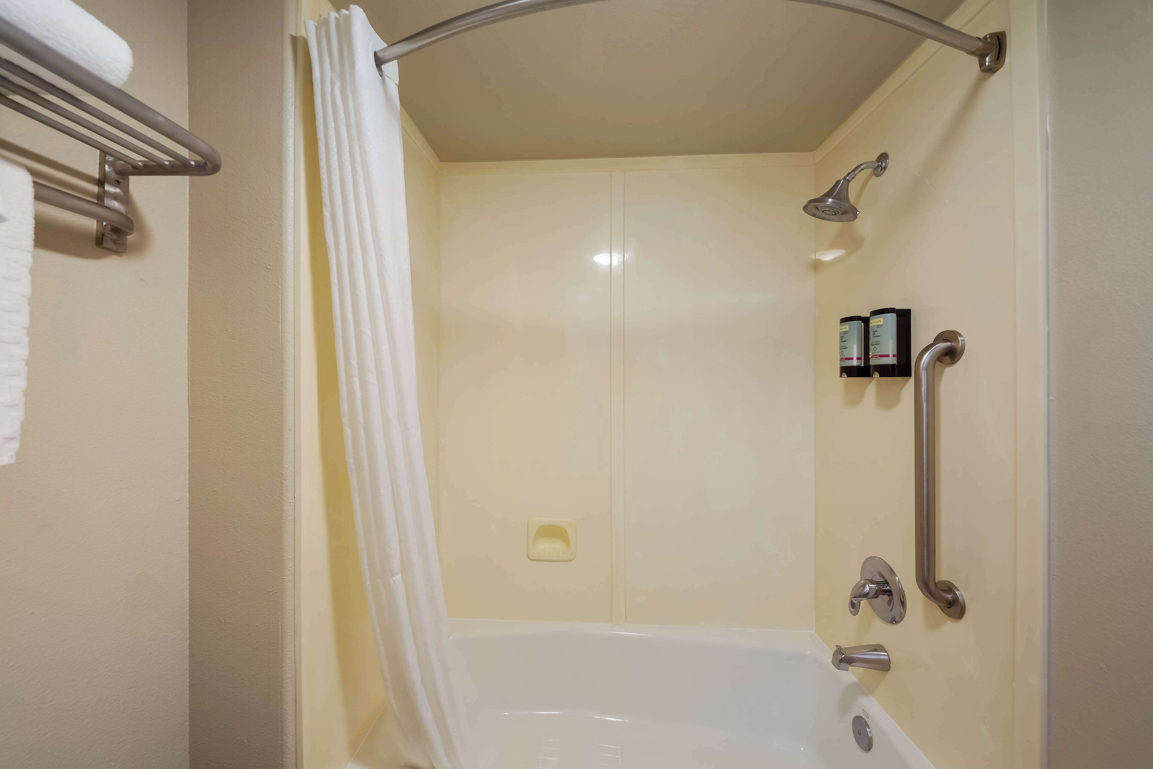 A shower area with a bathtub, a handrail, and a towel rack.