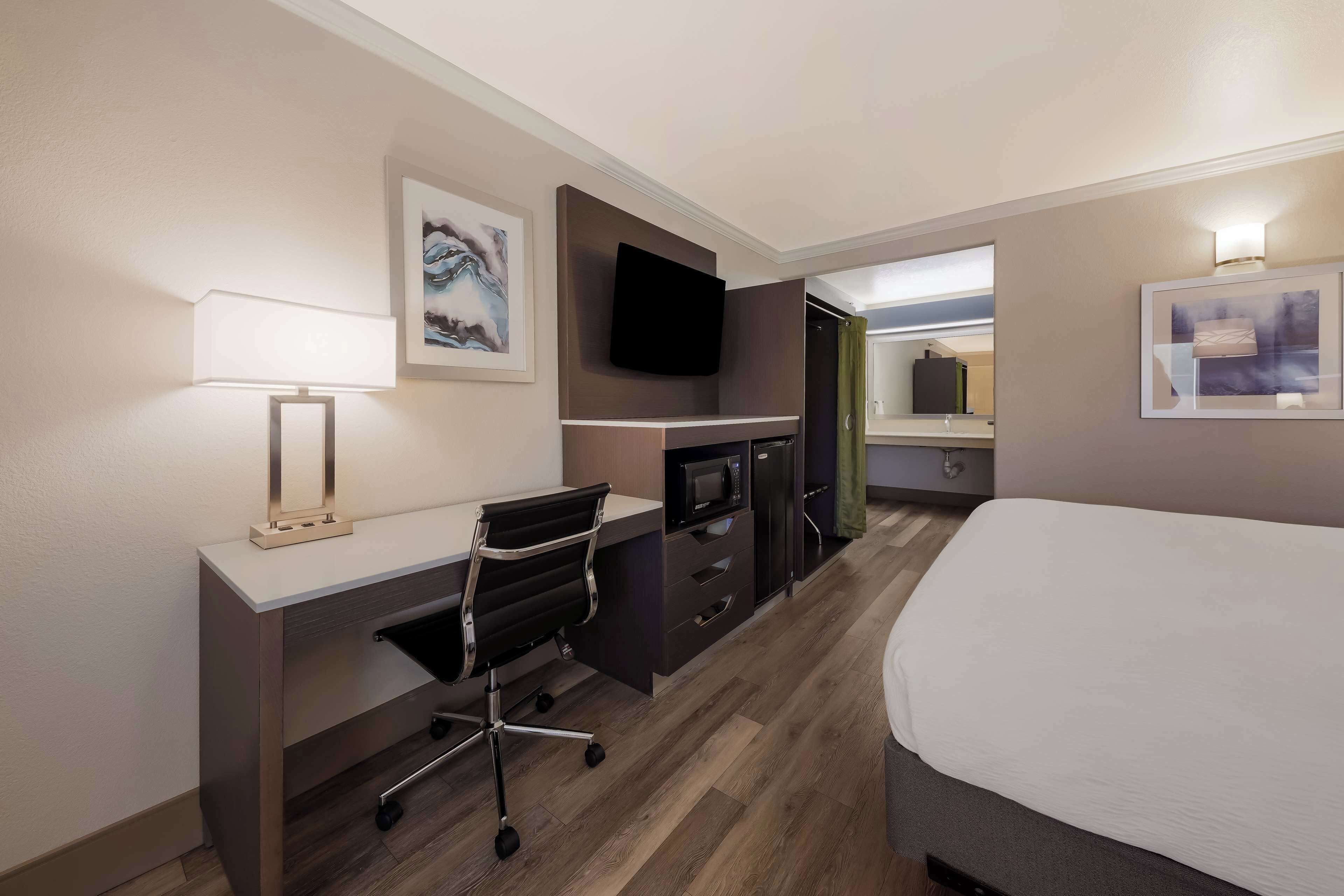 A hotel room with a bed, a desk with a chair, a flat-screen TV mounted on the wall, a microwave, and a small cabinet.