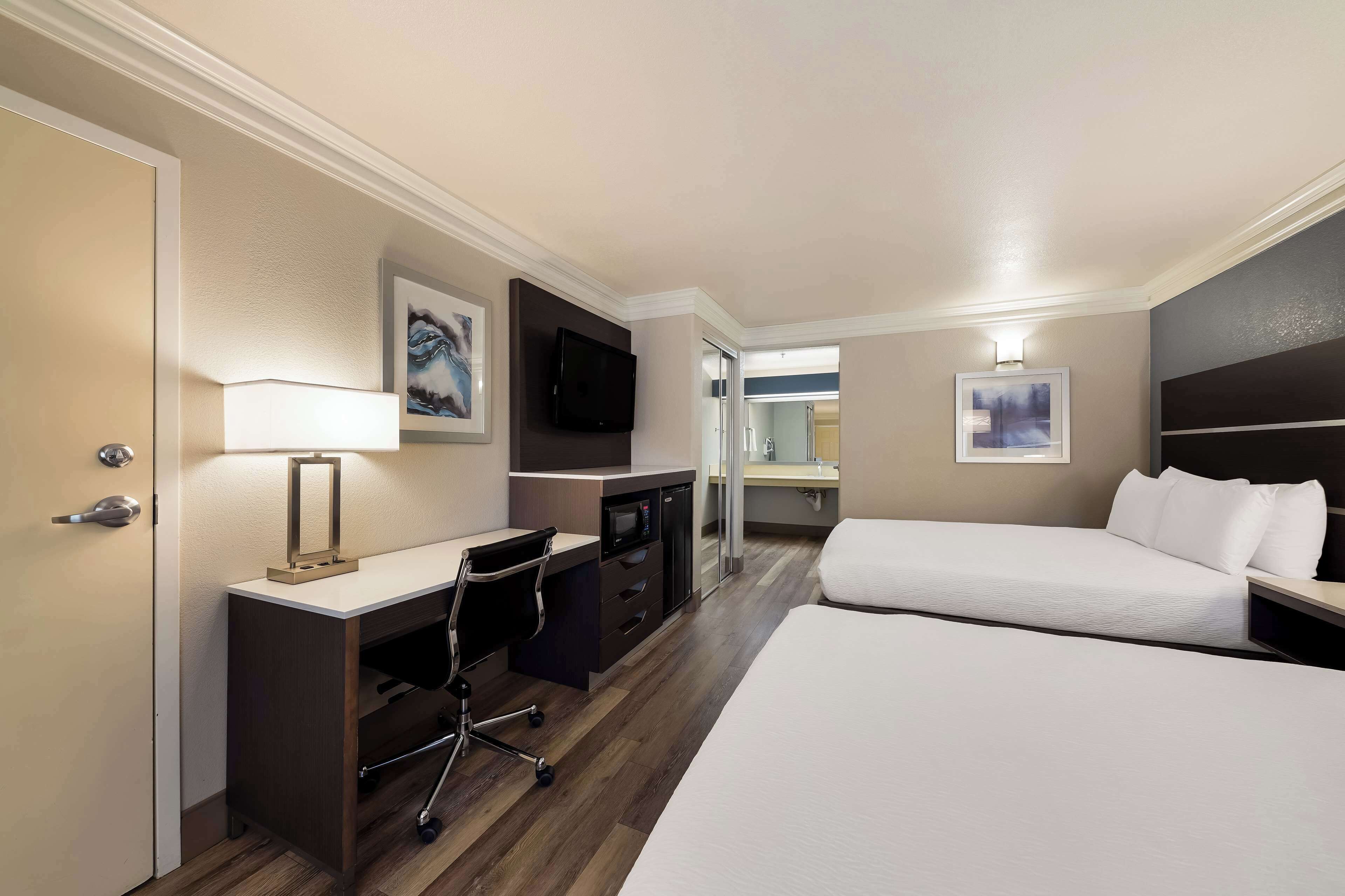 A hotel room with a desk, two beds, a TV, and artwork on the walls.