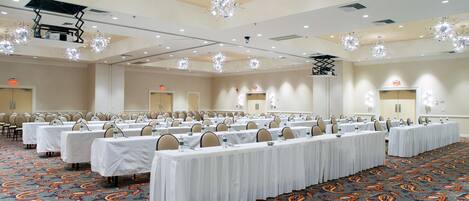 Een ruime conferentiezaal met rijen tafels, stoelen en kroonluchters.