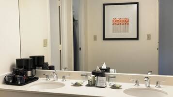 A hotel bathroom with two sinks, a coffee maker, and a framed artwork on the wall.