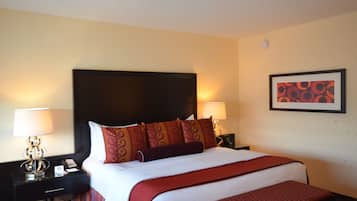 Habitación de hotel con una cama grande, dos mesitas de noche con lámparas, un cuadro enmarcado en la pared y un pequeño banco al pie de la cama.