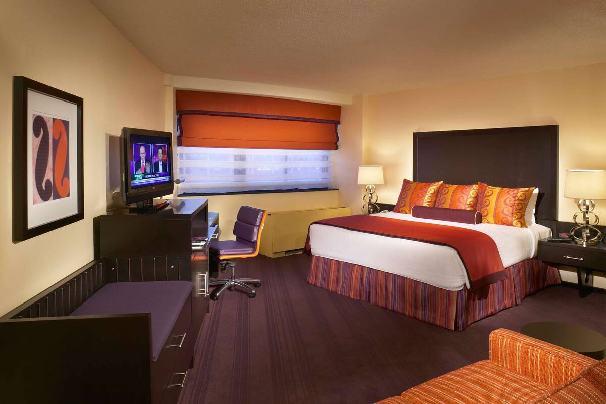 Quarto de hotel com uma cama grande, uma mesa com cadeira, televisão e janela com vista.