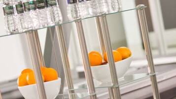 Una repisa de vidrio con botellas de agua, un cuenco de naranjas y toallas dobladas.