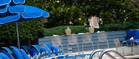 A poolside area with lounge chairs and umbrellas, a pool, and a building in the background.