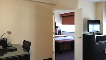 A hotel room with a bed, a desk with a lamp, a television, and a wardrobe.