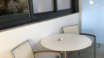 Una pequeña mesa redonda con dos sillas, un cartel sobre la mesa y una ventana al fondo.
