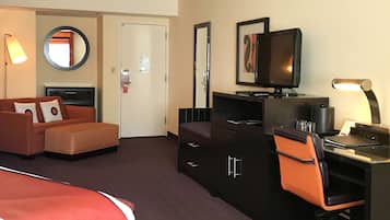 A hotel room with a bed, a desk with a computer, a chair, a TV, a dresser, and a mirror.