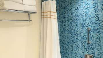 Un bagno con zona doccia caratterizzata da una parete in mosaico blu, un portascopevoli bianco e una tenda da doccia a righe arancioni.