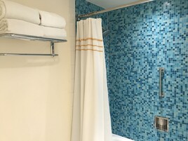 Une salle de bain avec un espace douche agrémenté d’un mur recouvert de mosaïques bleues, d’un porte-serviettes blanc et d’un rideau de douche à rayures orange.