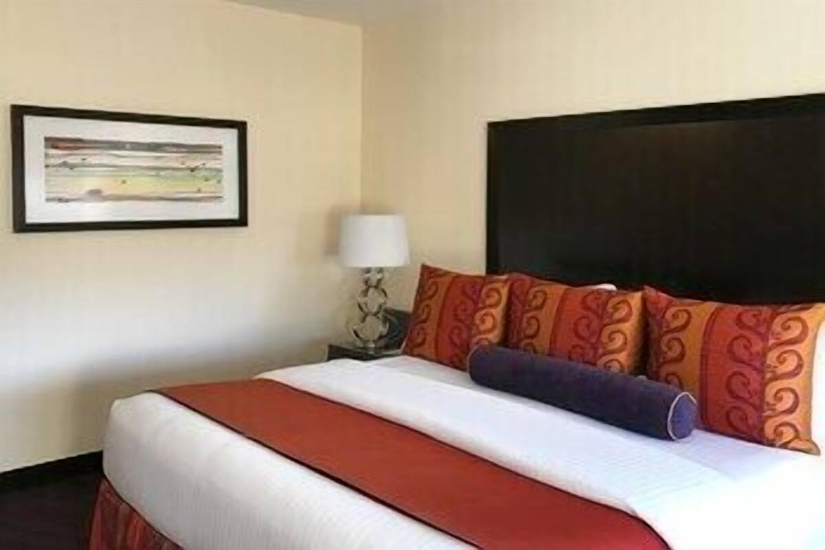 Quarto de hotel com uma cama, uma mesa de cabeceira, um abajur e um quadro na parede.