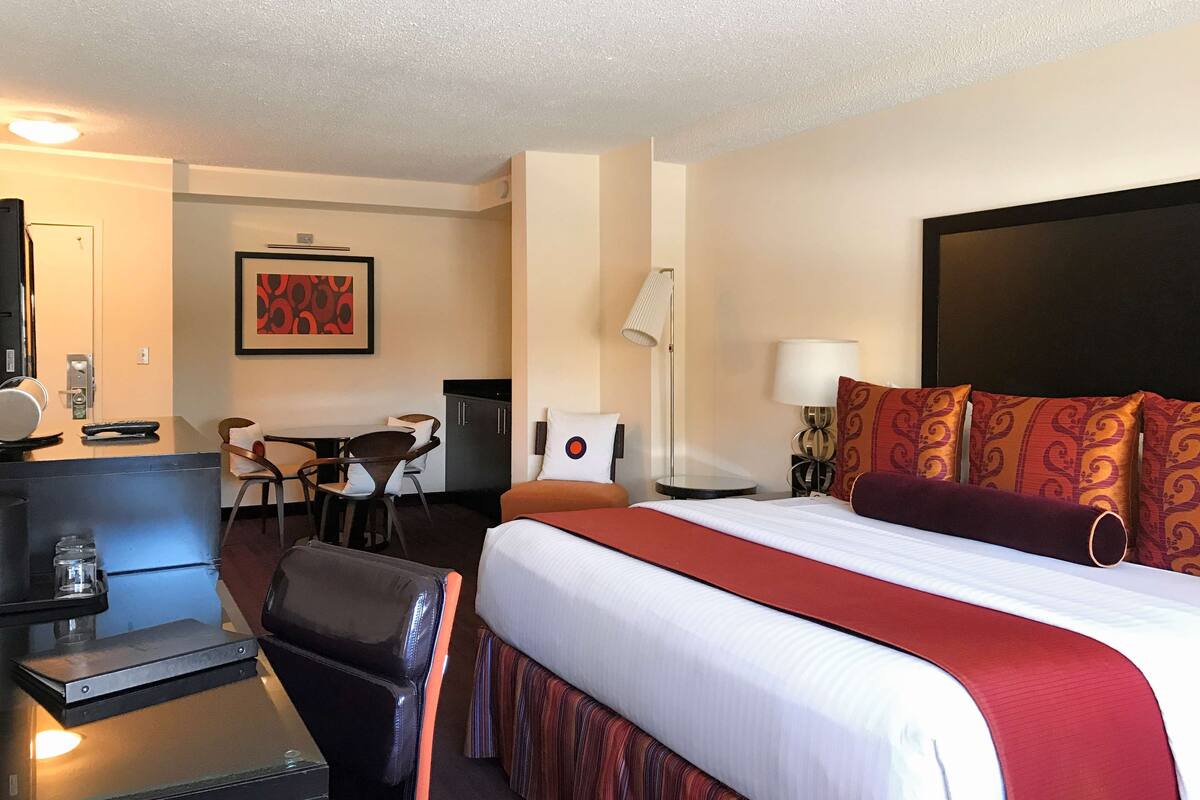 Quarto de hotel com uma cama grande, uma escrivaninha com computador, uma cadeira, abajur e um quadro na parede.