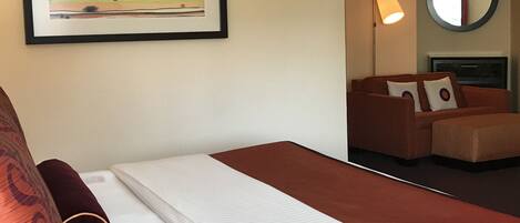 A hotel room with a bed, a sofa, a round mirror, and a framed artwork on the wall.