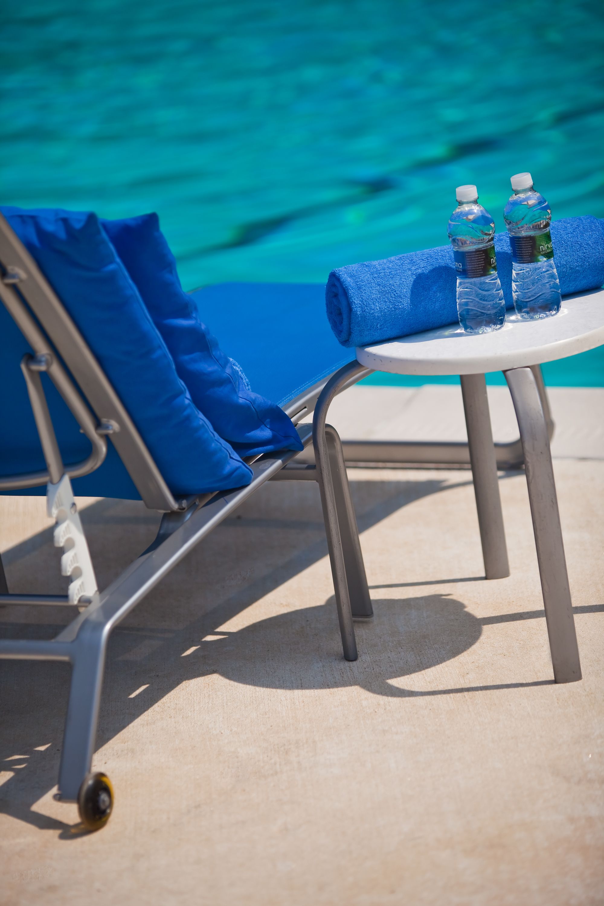 A poolside lounge area with a blue chair, a small round table, and two water bottles.