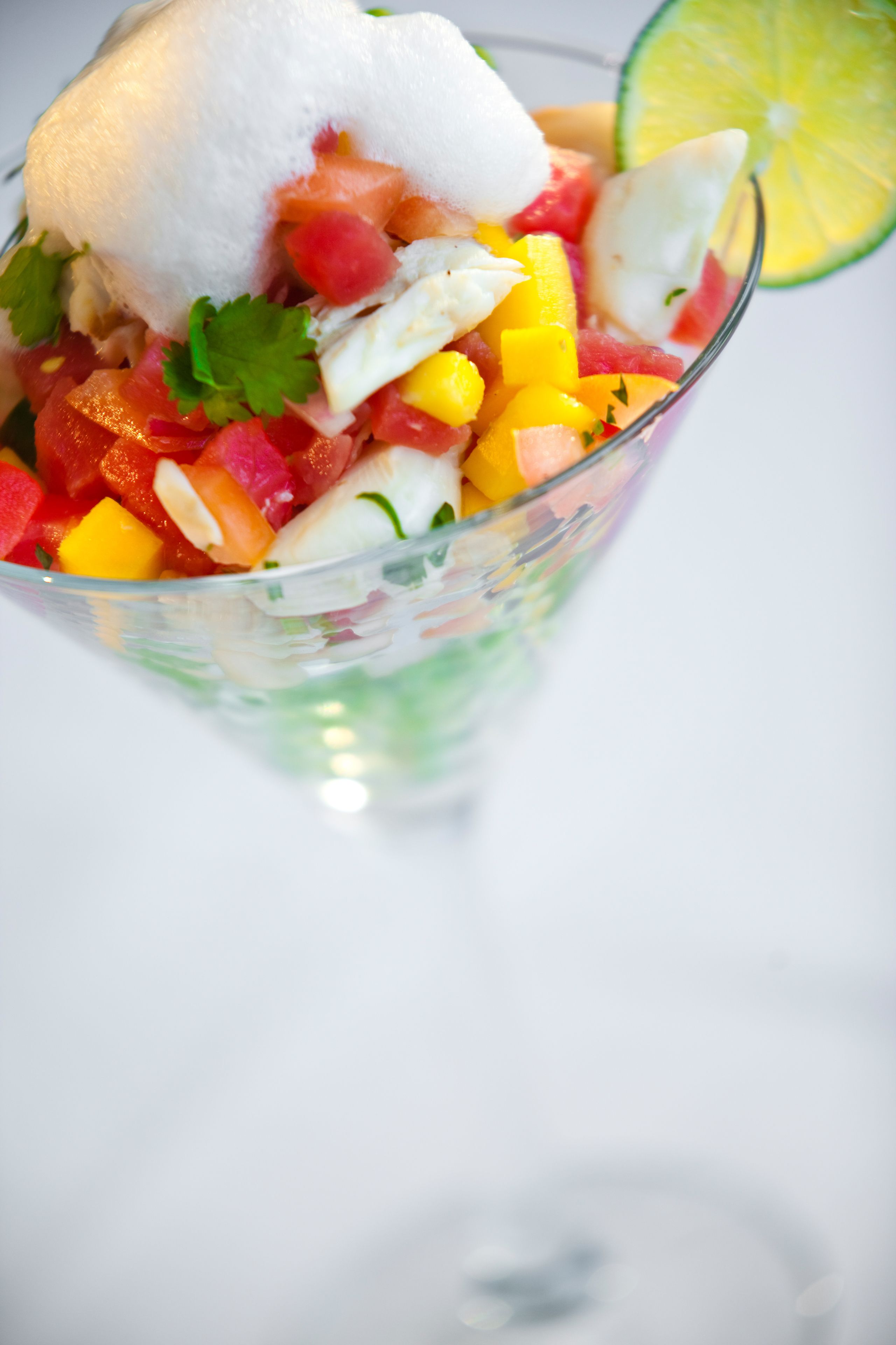 Eine transparente Glaskugel mit einem bunten Obstsalat, einem Klecks Sahne und einem Limettenschnitz.