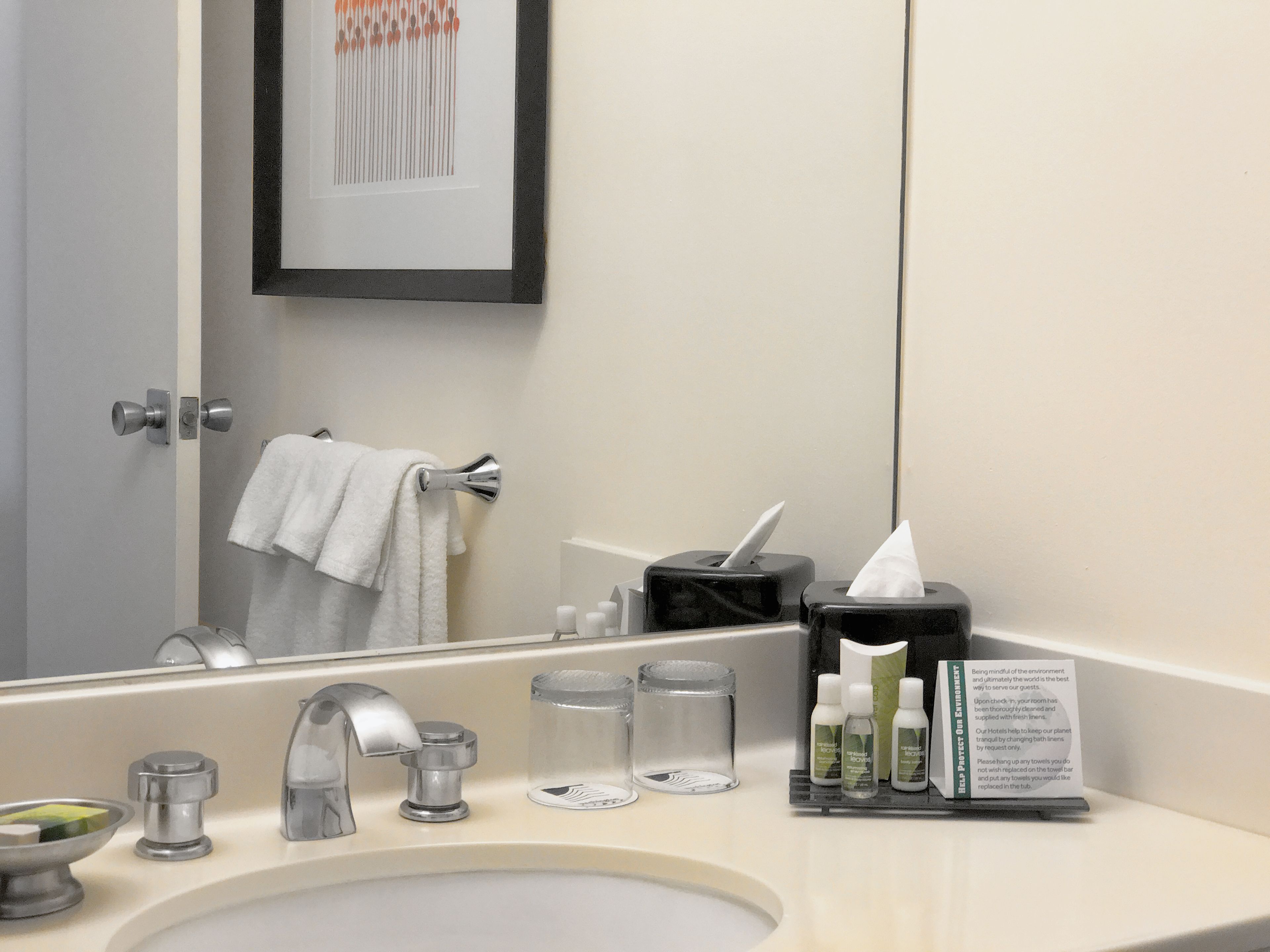 Une salle de bain d’hôtel équipée d’un lavabo, d’un miroir, d’un porte-serviettes et d’articles de toilette.