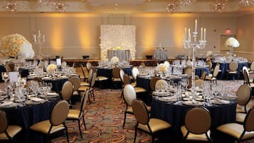 Un salón de banquetes con mesas redondas dispuestas para comer, con candelabros y centros de mesa florales.