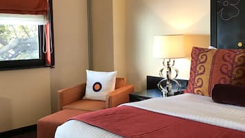 A hotel room with a bed, a chair, a nightstand, a lamp, and a window with curtains.