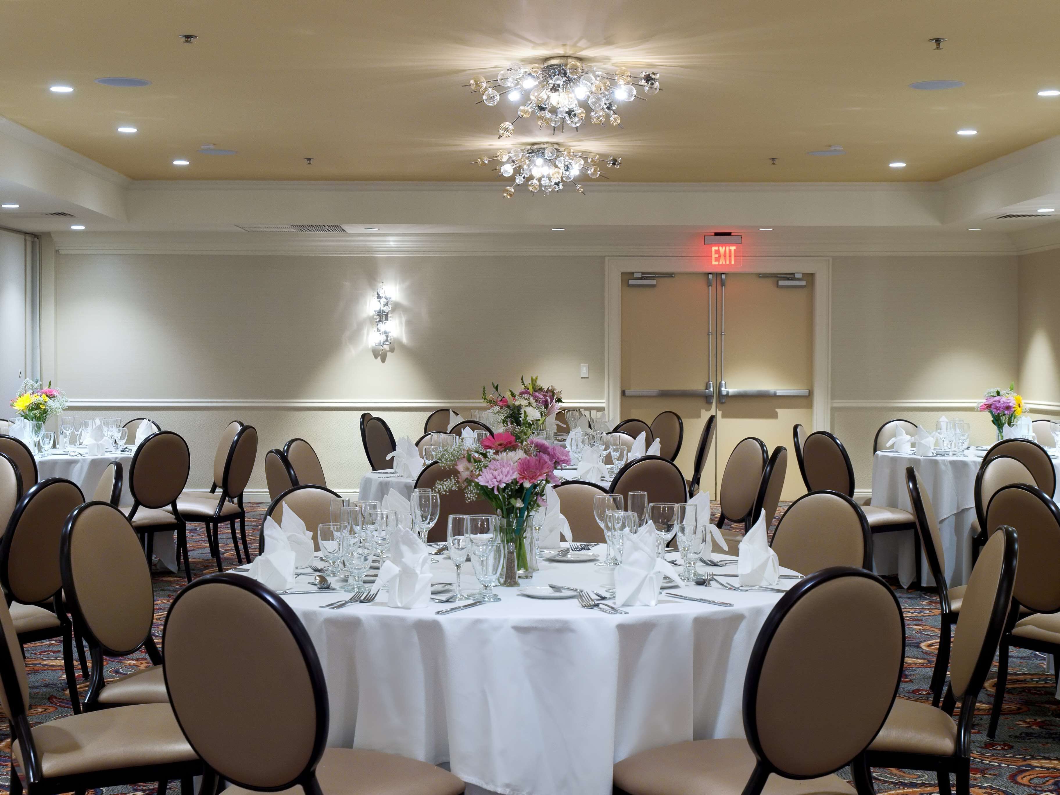 A banquet hall with round tables set for dining, chairs, and a chandelier.