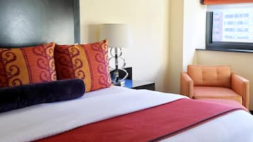 A hotel room with a large bed, a chair, a lamp, and a window with a view of buildings.