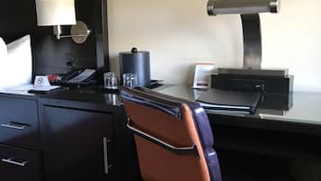 A hotel room with a desk, a telephone, a lamp, a printer, and a chair.