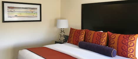 Una cama bien tendida con una colcha rojo y blanco, cabecera negra y almohadas estampadas.
