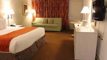 A hotel room with a bed, a green sofa, a desk with a lamp, and a television.